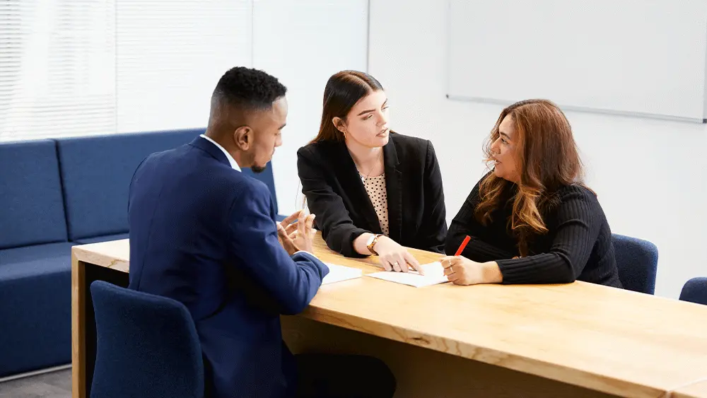 3 people sat at a desk with two of them offering advice