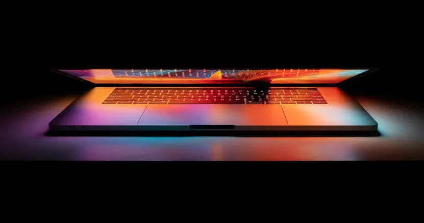 A laptop with a partially closed lid, with the screen reflecting on the keyboard.