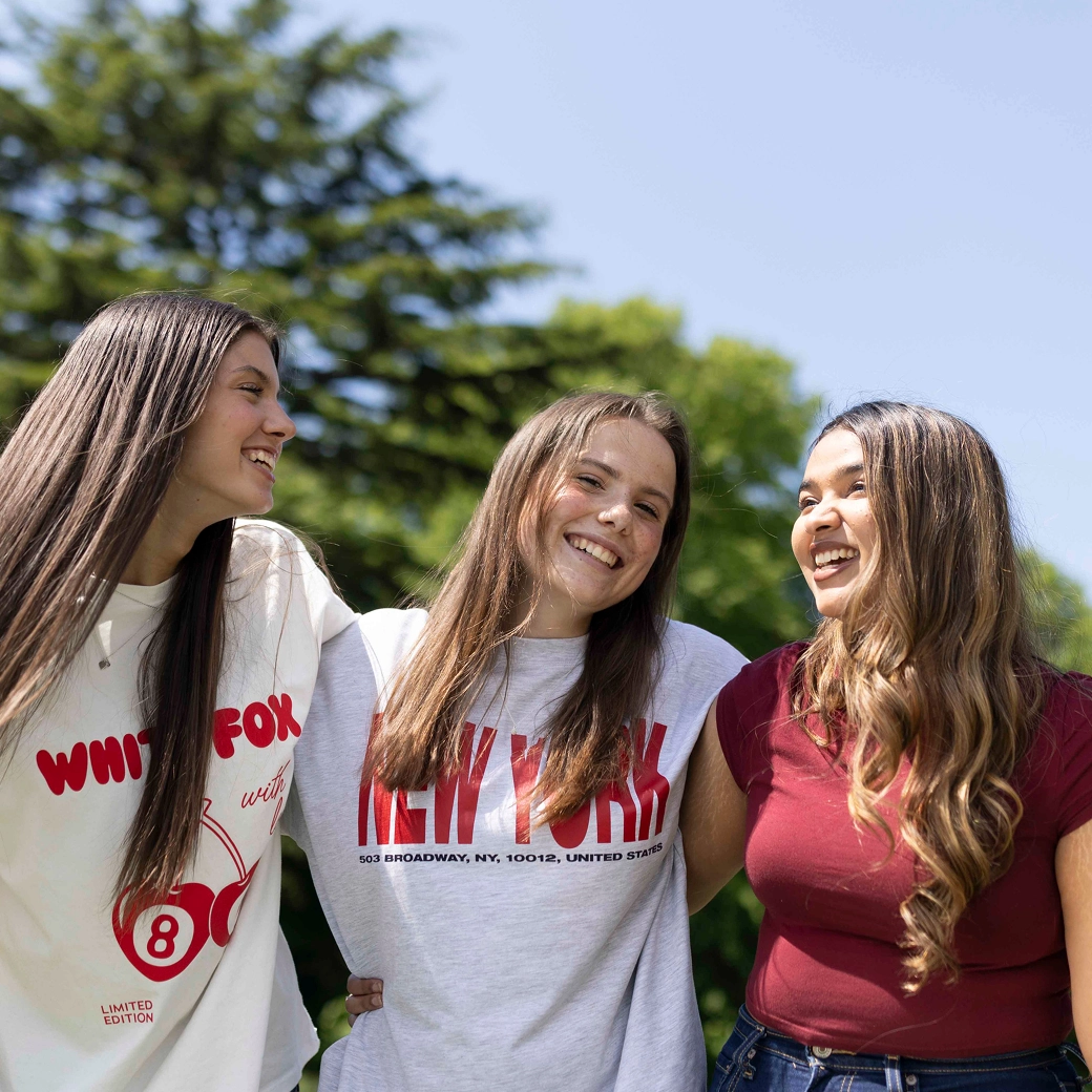 Three female students laughing with each other on a sunny day