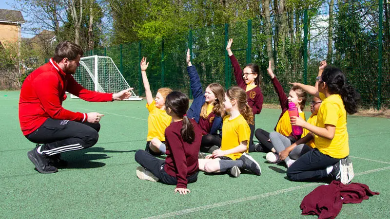 A Solent sport student with some school children on a sport pitch