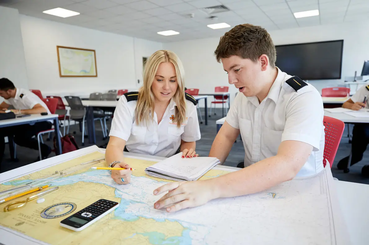 A boy and a girl sit at a desk and look at the colourful map on it.