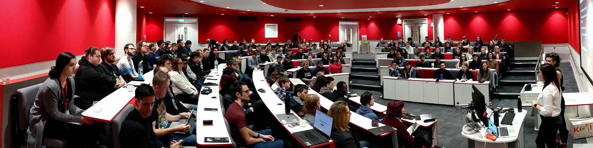 A lecture hall with 50 or so students sat down looking at two women stood up speaking.