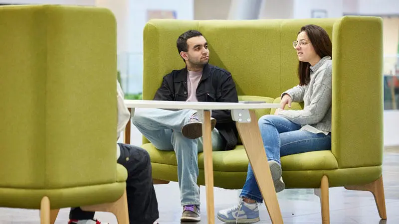 Students sat on green seats in the Spark, talking to each other