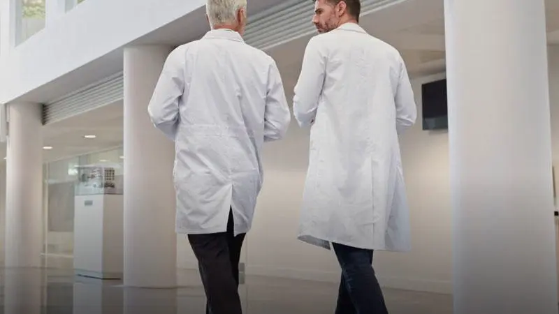 Two male health workers wearing white lab coats walking through The Spark