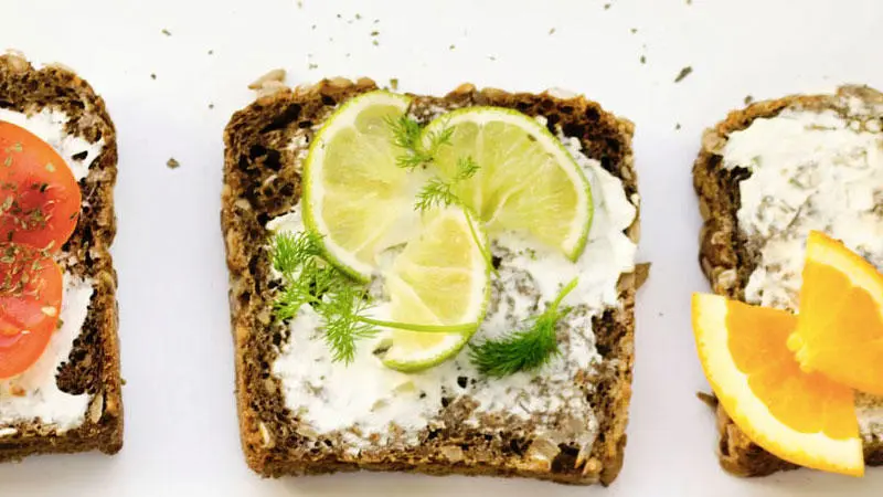 Three slices of toast next to each other with cream cheese, tomato and fruit.