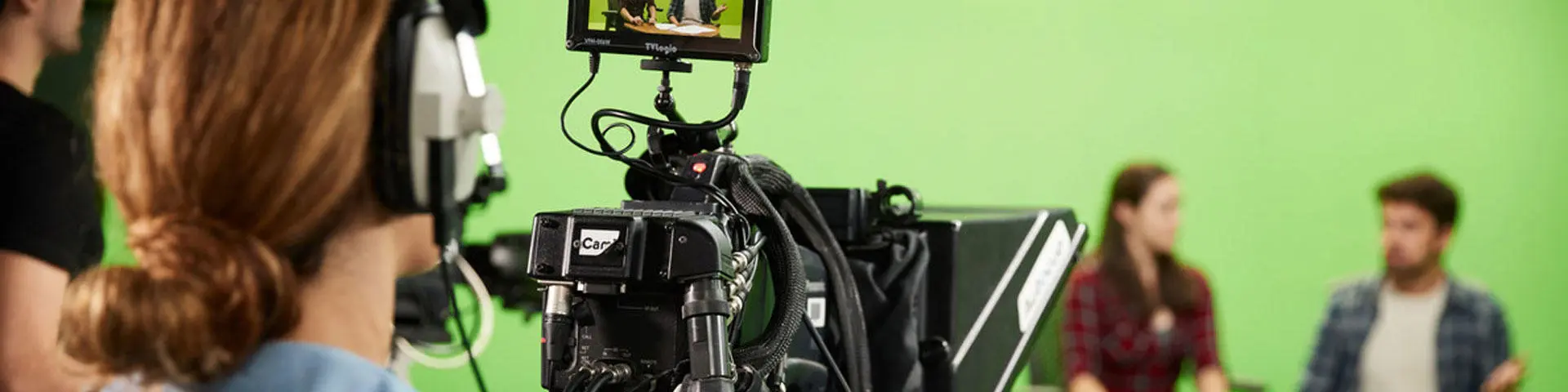 A student stood behind a television camera filming people on set