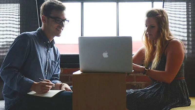 Two people sat down looking at laptop screen.