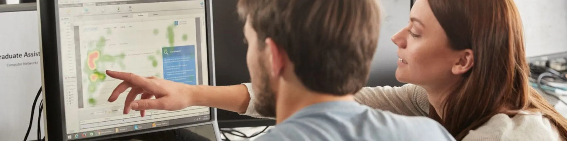 A woman points at a computer screen which a man looks at.