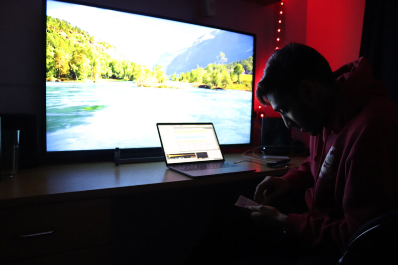 Avi at his desk with a large TV and laptop