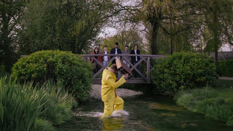 Fred Lane standing on a bridge watching someone in a river, dressed in yellow with a briefcase