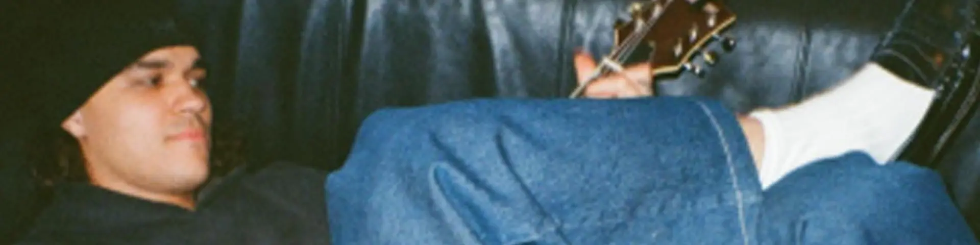 A guy laying down playing a brown guitar on a sofa