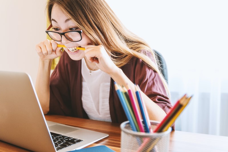 A girl sat in front of a laptop looking stressed and chewing a pencil