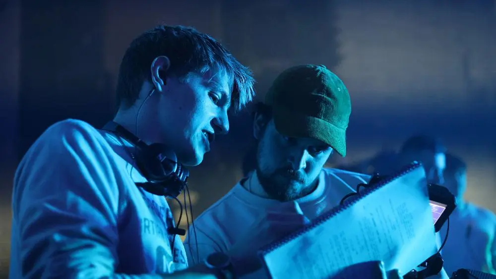 Liam Calvert with Oliver Bury, looking at a script on a film set.