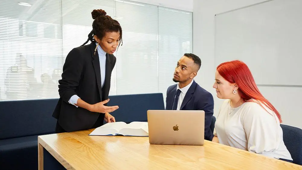 Two women and a man sat around a laptop in an office.