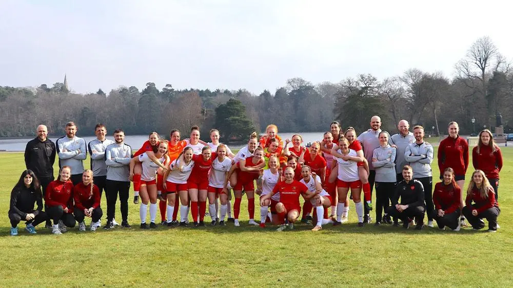 A group photo in a field by a lake of the British Army women's football team.