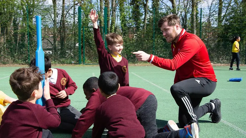 School children taking part in sport outside with a Solent student. 