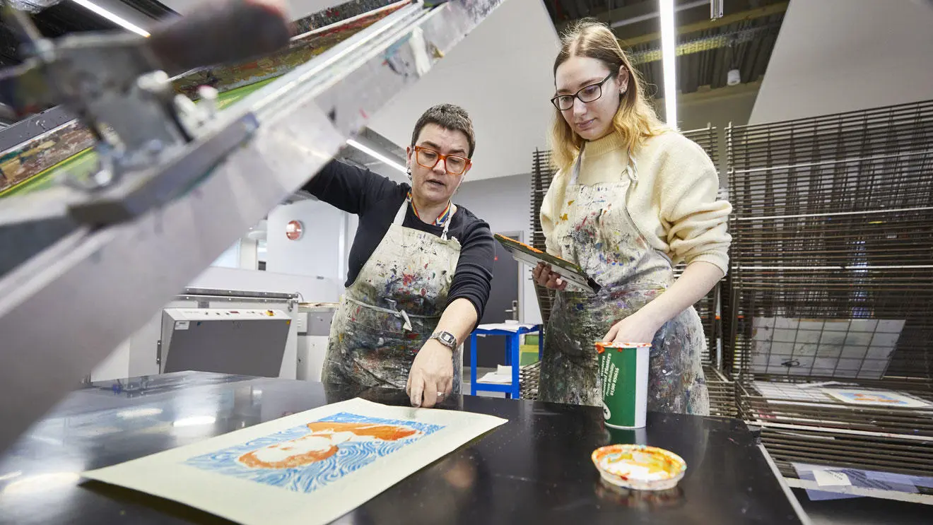 An illustration student with a technician using a screen printer