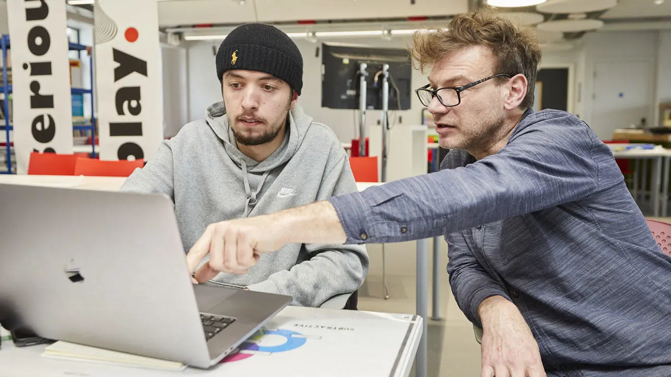 A graphic design student with a technician looking at a laptop