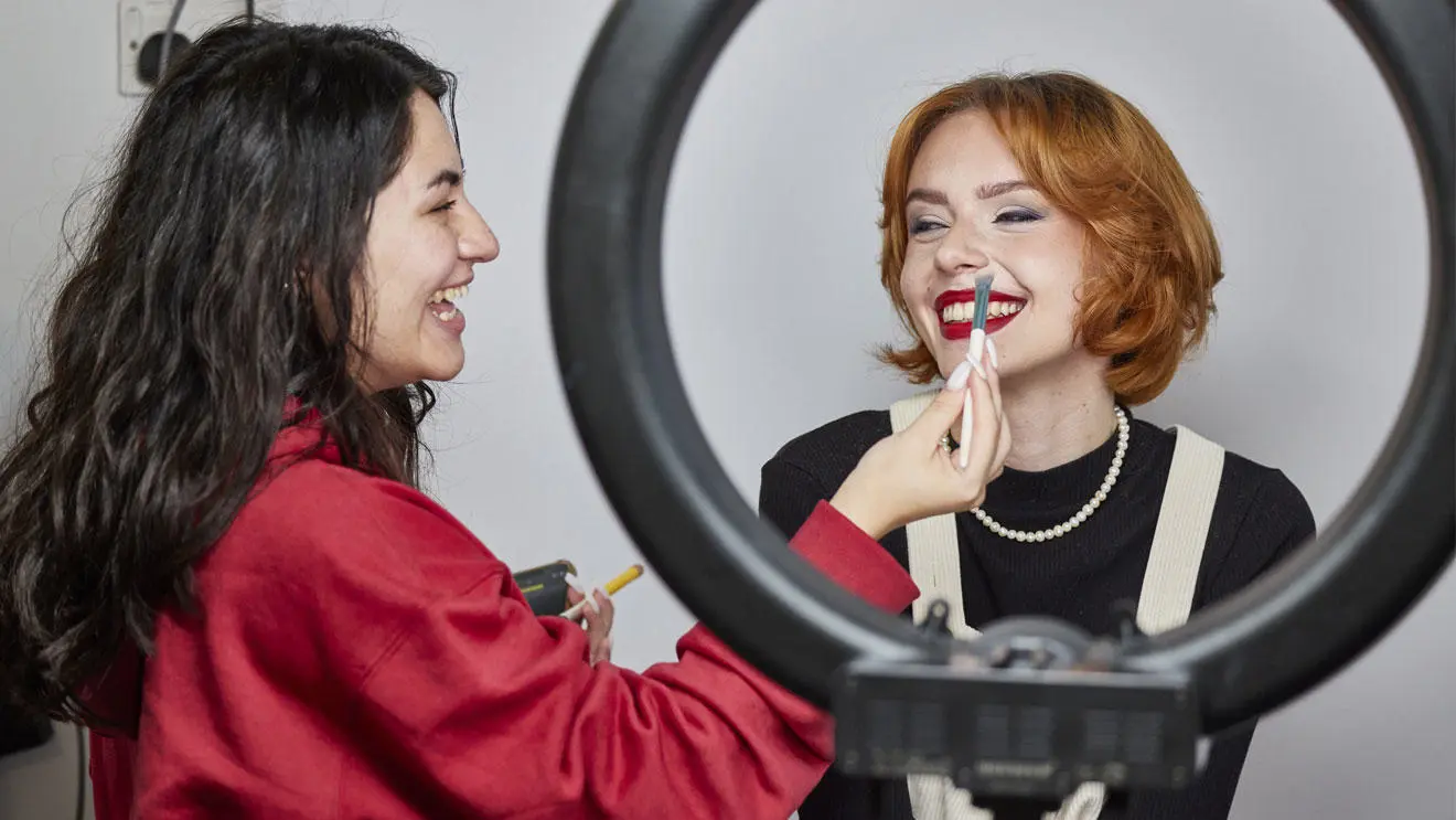 A make-up student applying concealer to a smiling model