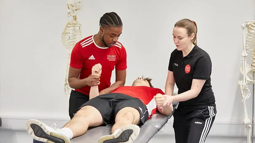 Two people working with a client providing therapy in a sport setting