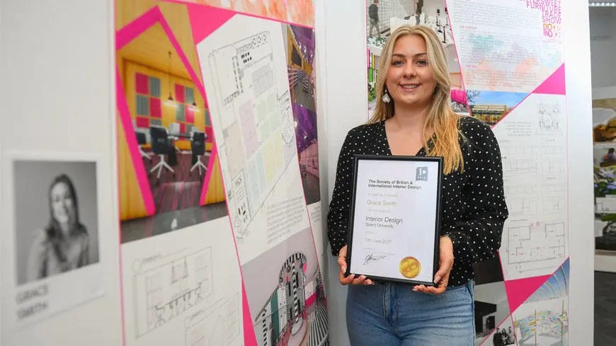 An interior design student stood in front of her work and holding a certificate