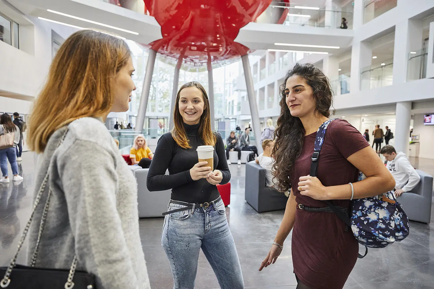 Three female students talking to each other in the Spark with the Pod in the background