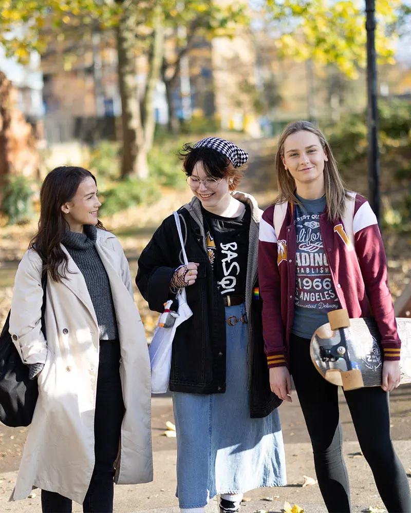 Three female students walking through a park