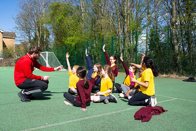 A solent sport student working with a group of school children who are all raising their hands