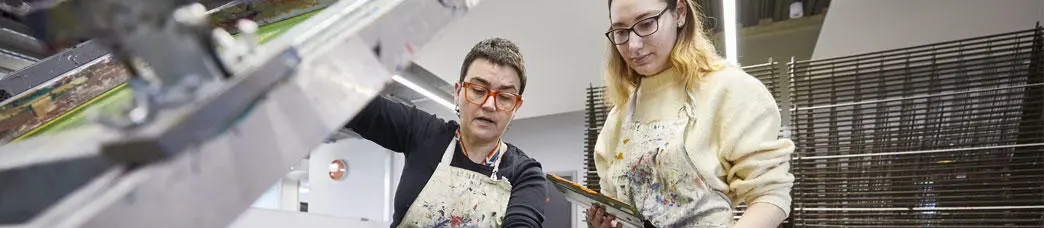 An illustration student with an instructor using the screen print press